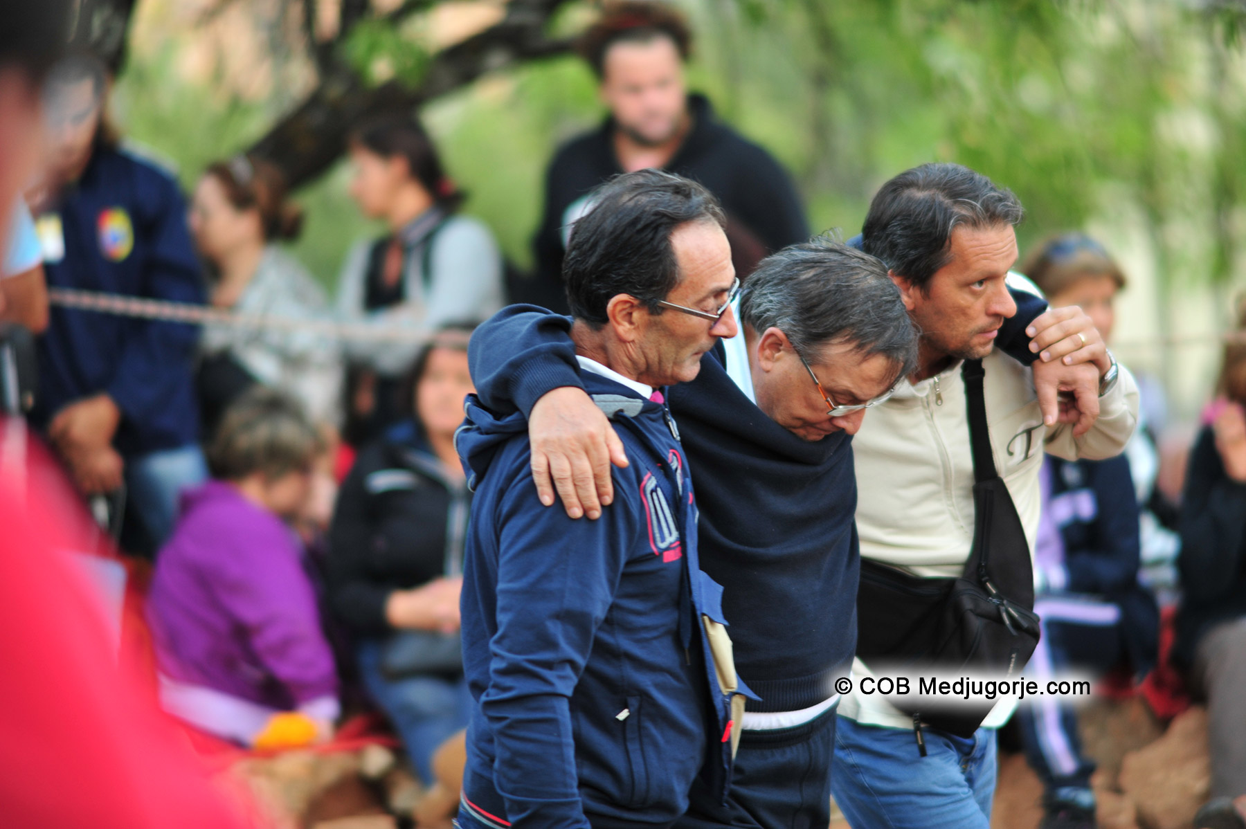 two men carry a crippled man to apparition of Our Lady of Medjugorje